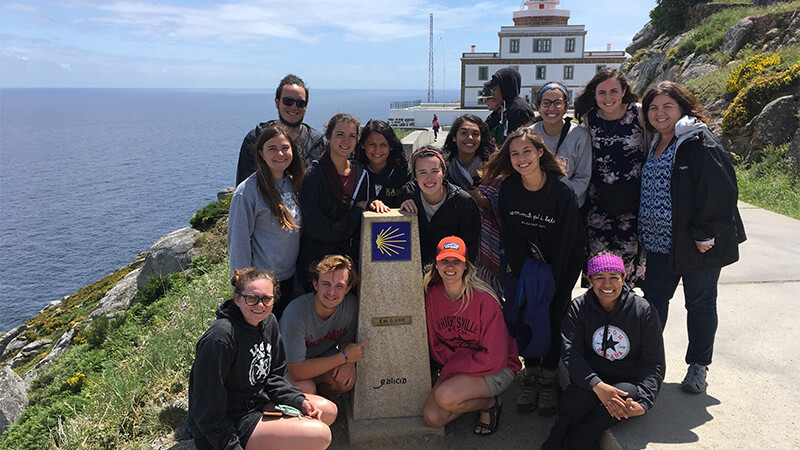Traveling student group pauses for a photo at an overlook with ocean in background.