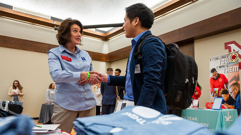 Student talks and shakes hands with corporate participant at career fair. 