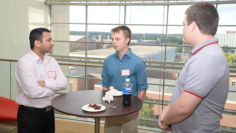 Student speaks with two faculty around small table.