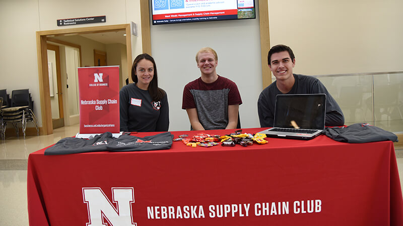 Three students sit at table for Supply Chain Club.