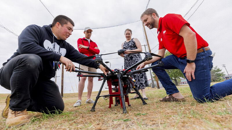 Students and instructors examine and discuss a drone.
