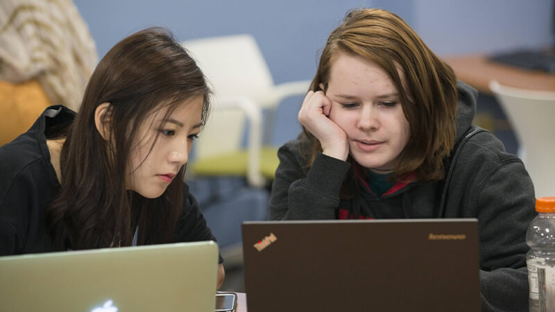 Two students look at laptop screen.