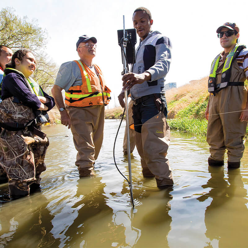 Students holding testing equipment while wading in water