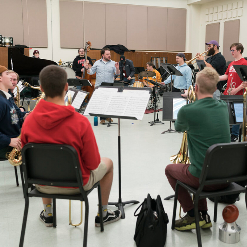 Student musicians sit in a circle and listen to instruction from the professor