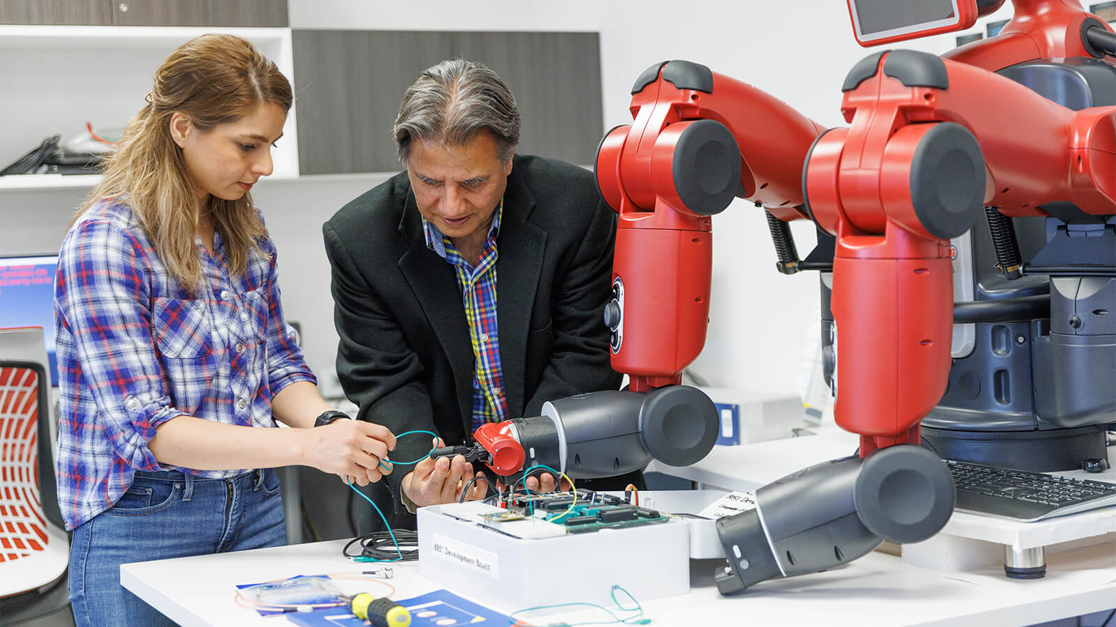 Student and professor work together in robotics lab; with red robotic arms at right.