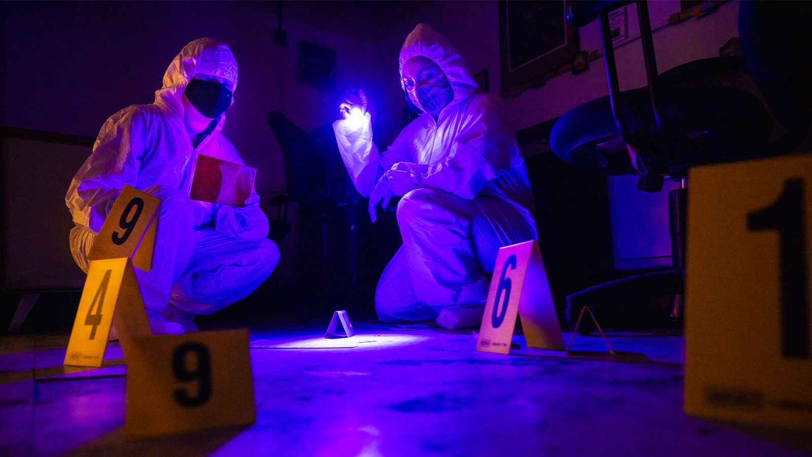Two student researchers examine a mock crime scene under ultraviolet light