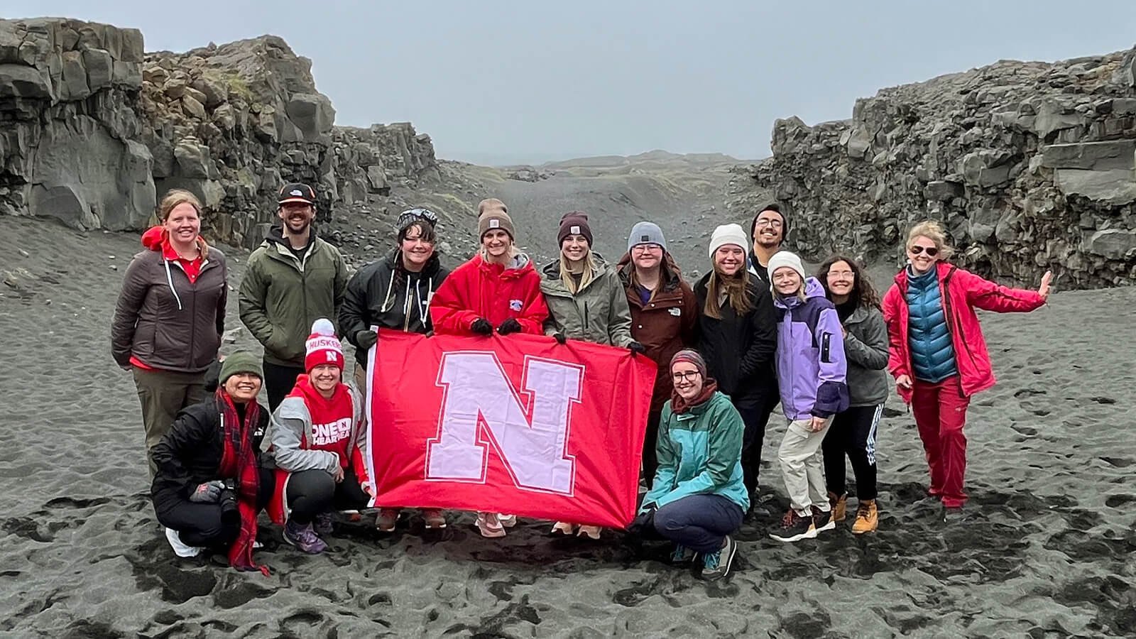 A group of students hold up a red Nebraska flag on rocky terrain