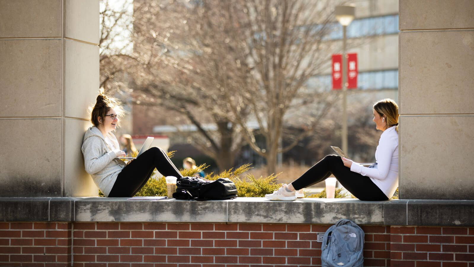 Two students talk between a building's columns on a bright spring day