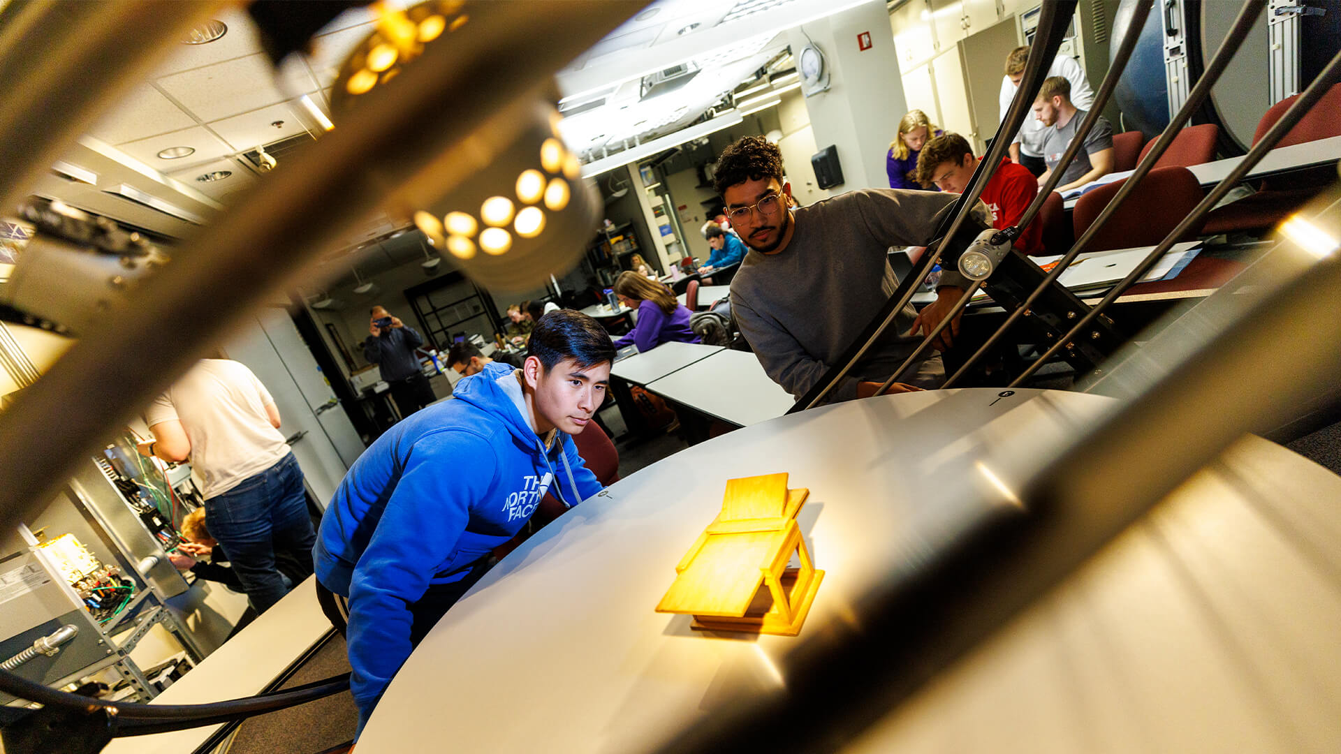 Students look at small wood model on display table