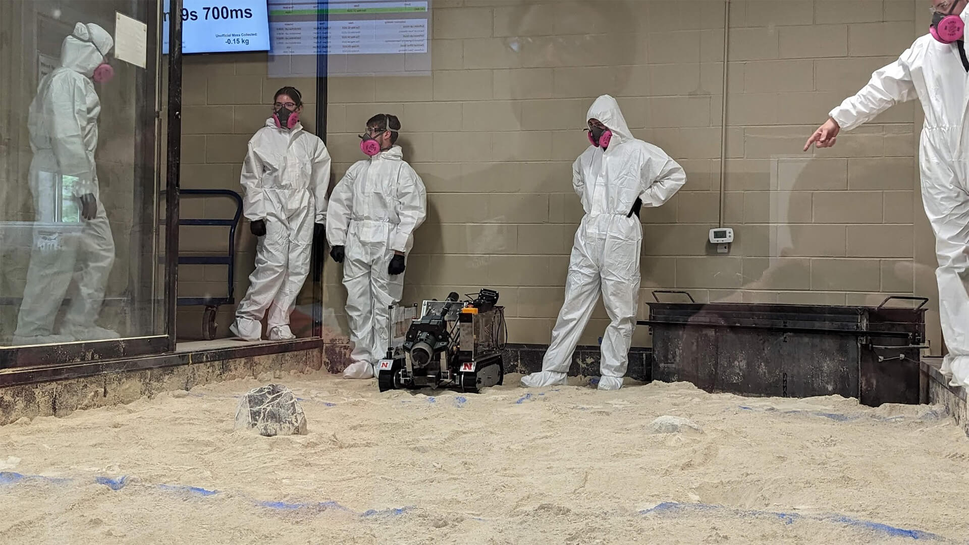 Students in dust suits watch as autonomous robot navigates sand pit