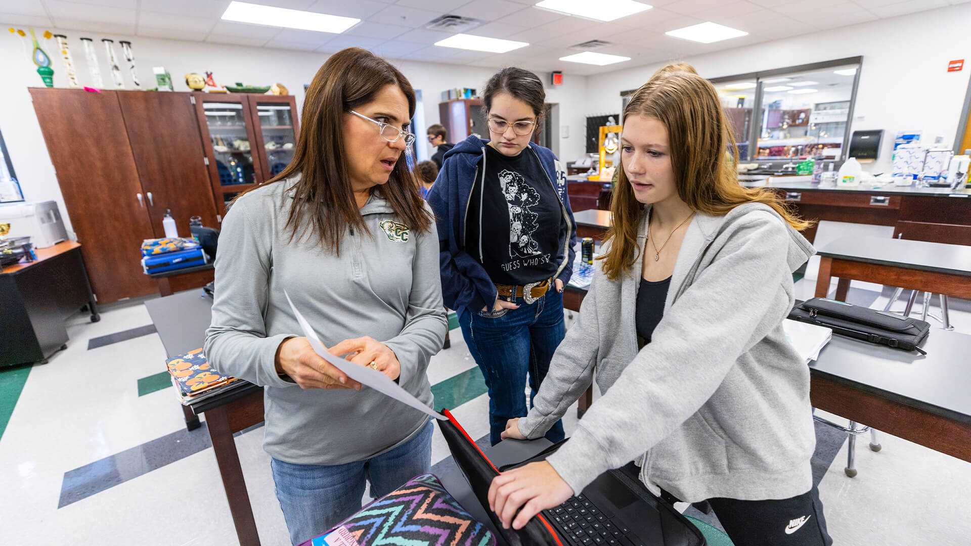 Professor talking to students while looking at laptop