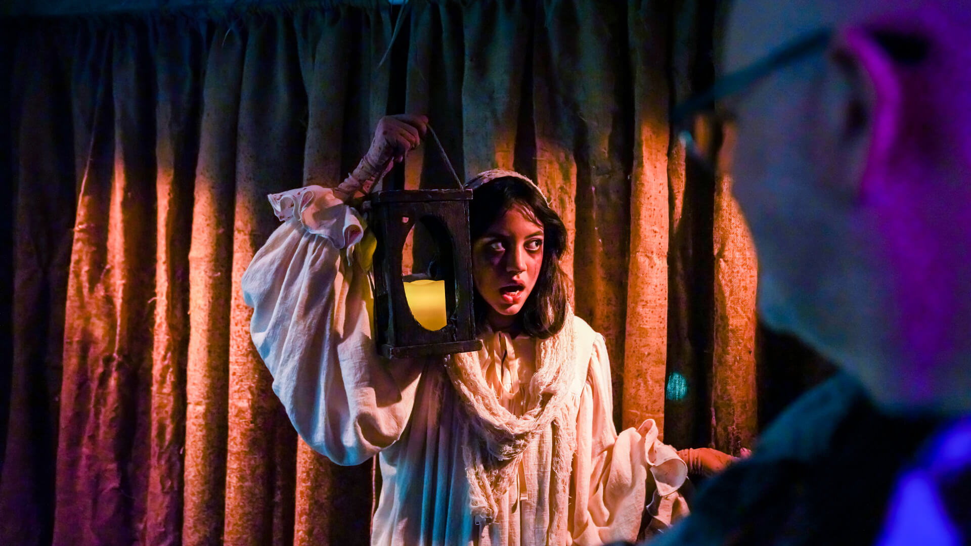 Student holding lantern while wearing robe in theater production
