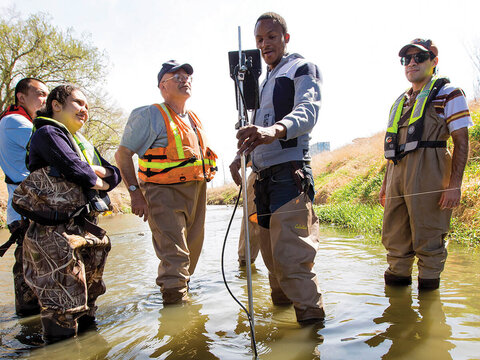 Students with water testing equipment wearing waders in water