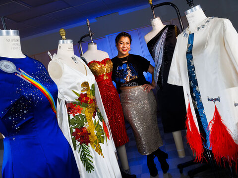 Student designers stands among colorful dresses mounted on mannequins.
