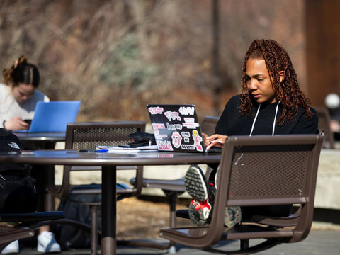 Student works on a laptop while sitting outside at a table