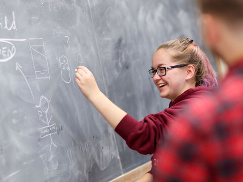Woman at chalkboard writing in German.