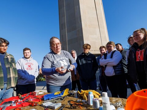 A professor and students inspect items on a table outside on campus.